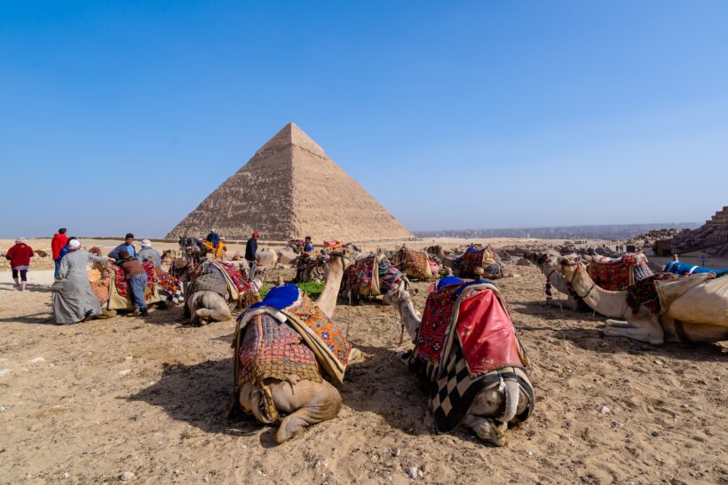 people sitting on brown sand near pyramid under blue sky during daytime